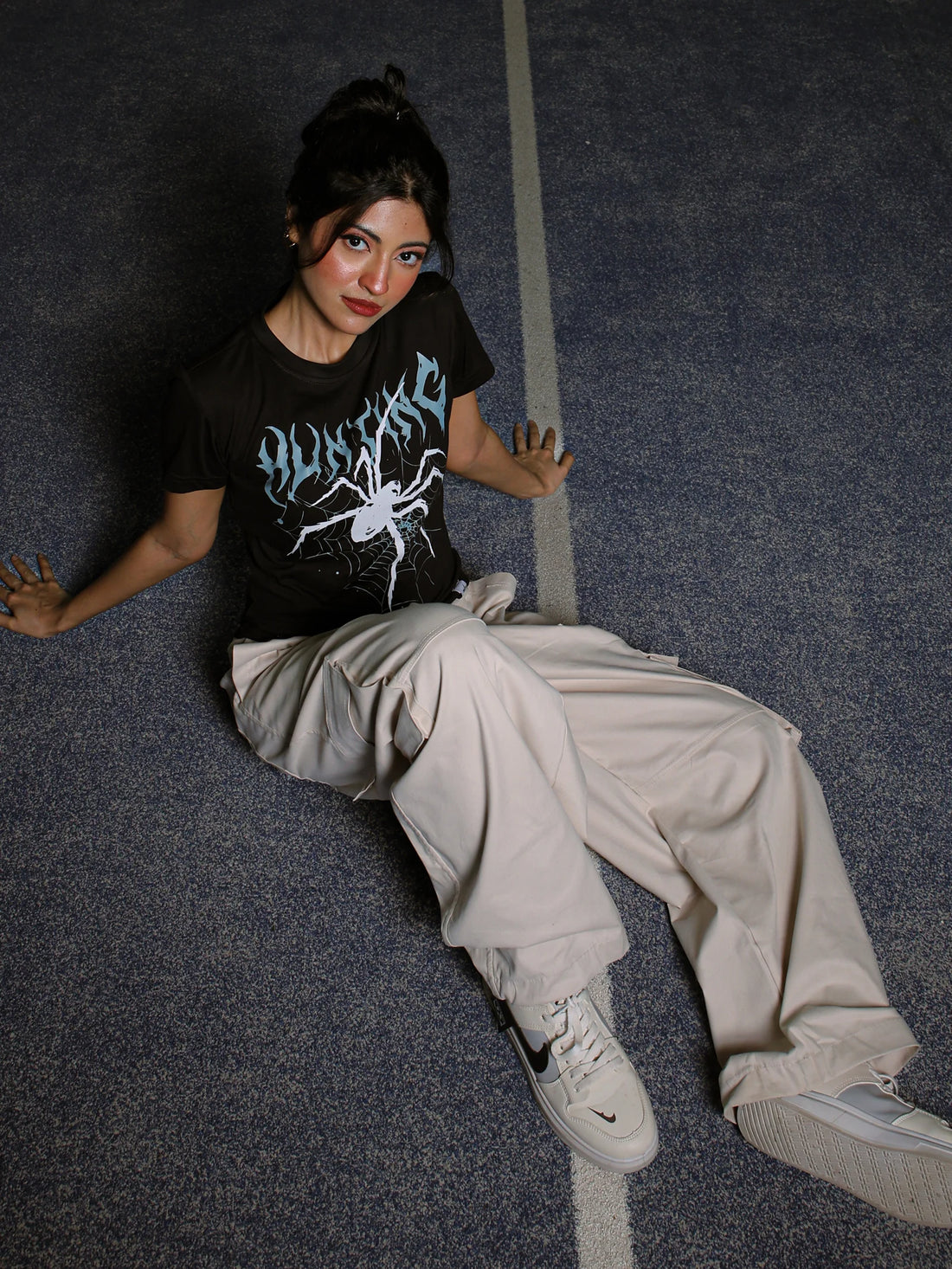 Person wearing a black t-shirt with graphic design and light-colored pants sitting on a dark floor.