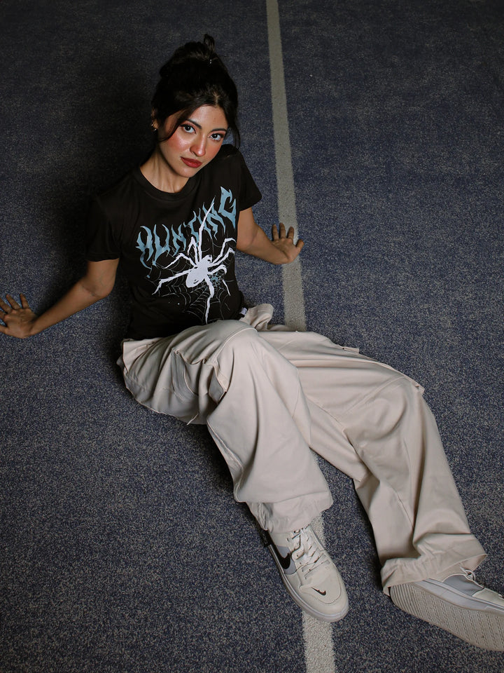 Person wearing a black t-shirt with graphic design and light-colored pants sitting on a dark floor.