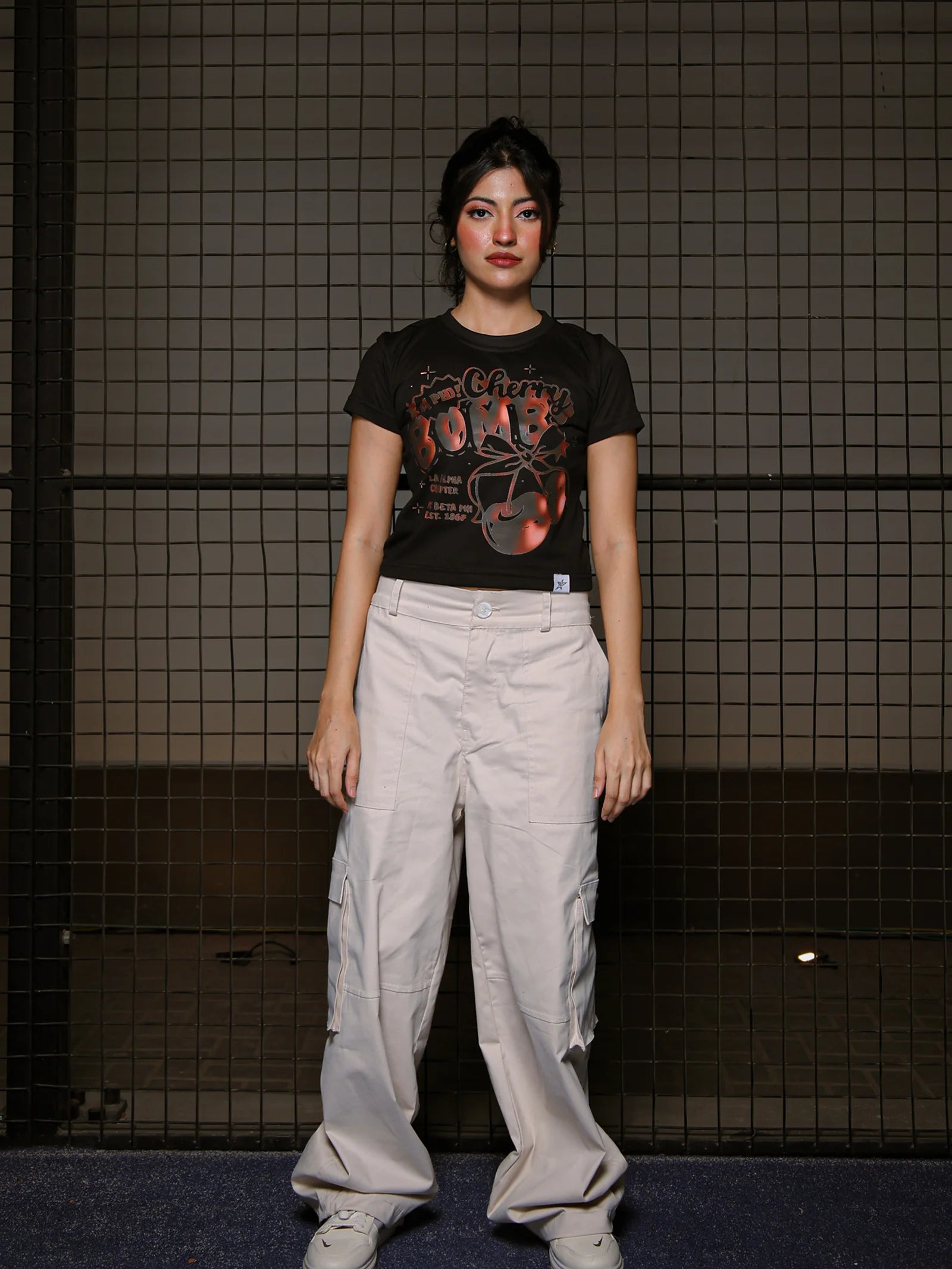 Person wearing a black t-shirt with graphic design and light-colored pants against a tiled wall.