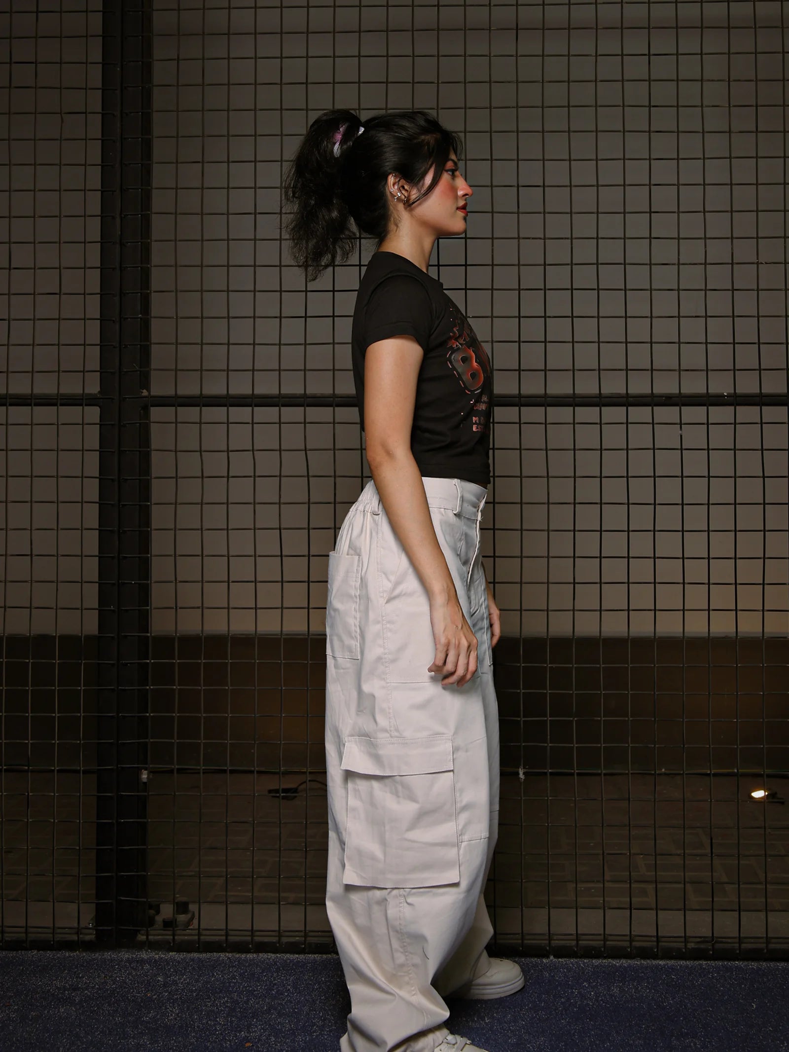 Person wearing a black top and light gray pants standing against a tiled wall.