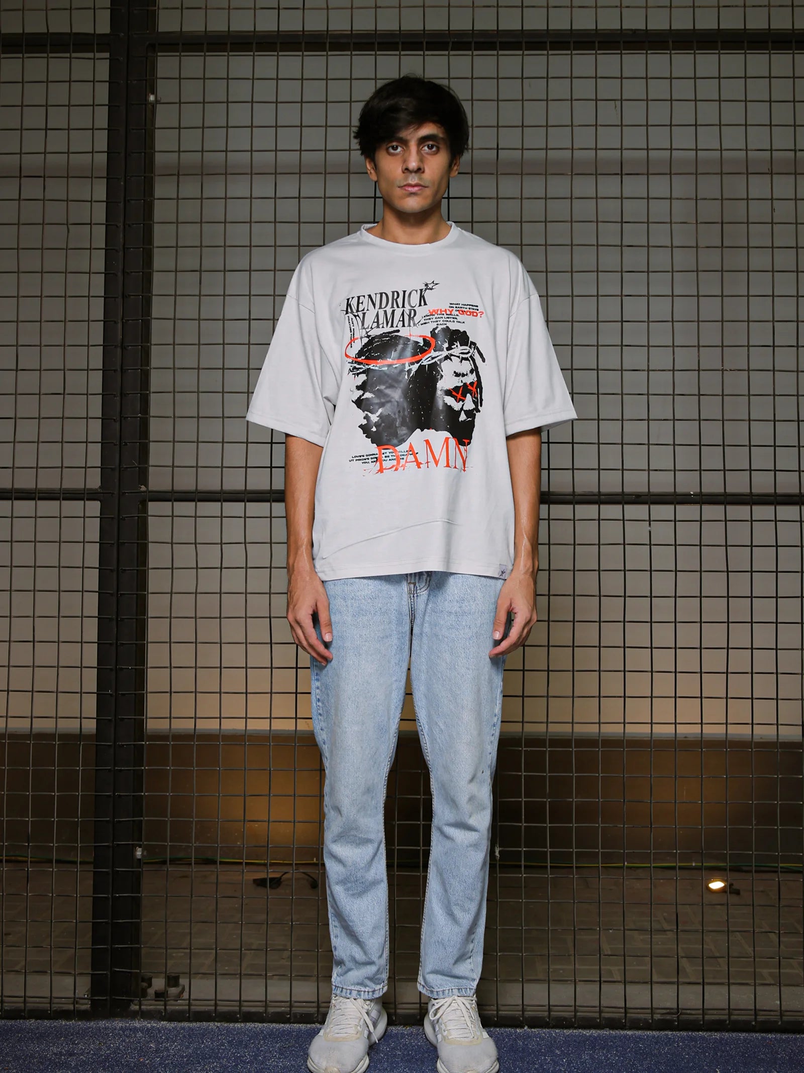 Person wearing a graphic t-shirt and jeans standing against a grid-patterned wall.