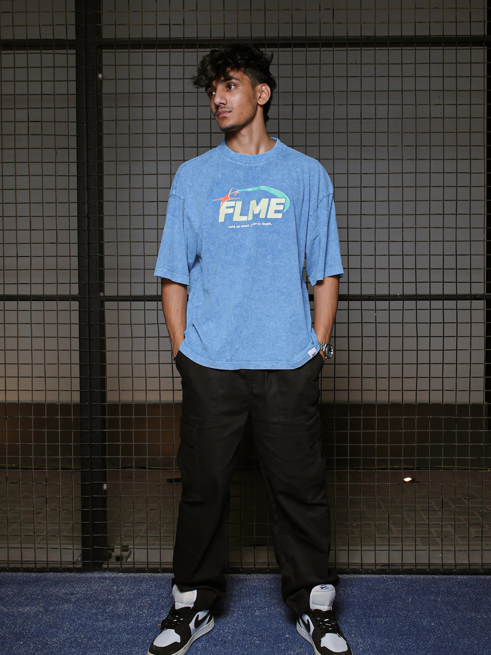Person wearing a blue t-shirt with 'FLME' logo against a grid-patterned wall.