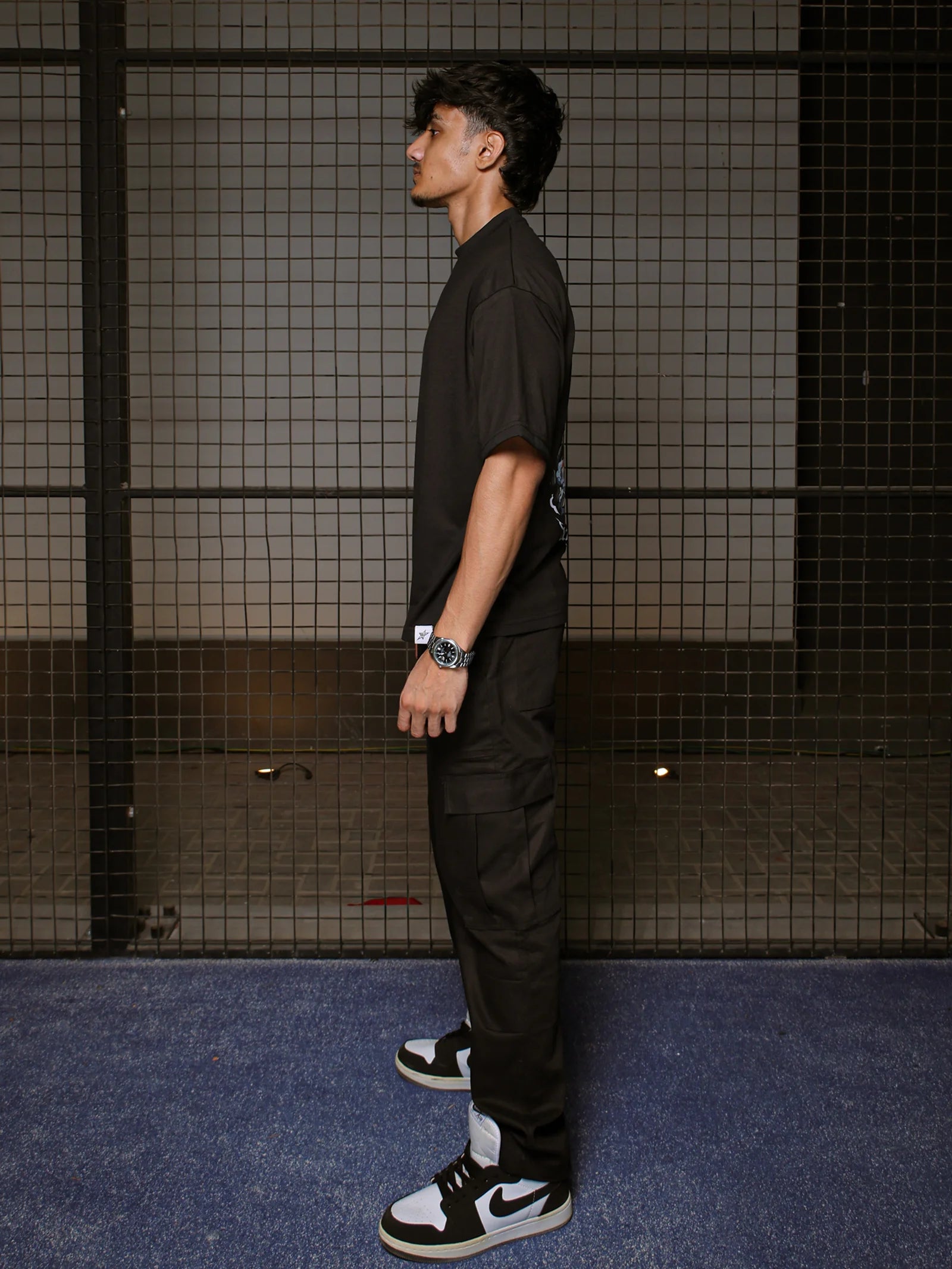 Person wearing a black outfit with a Nike sneaker standing against a tiled wall.