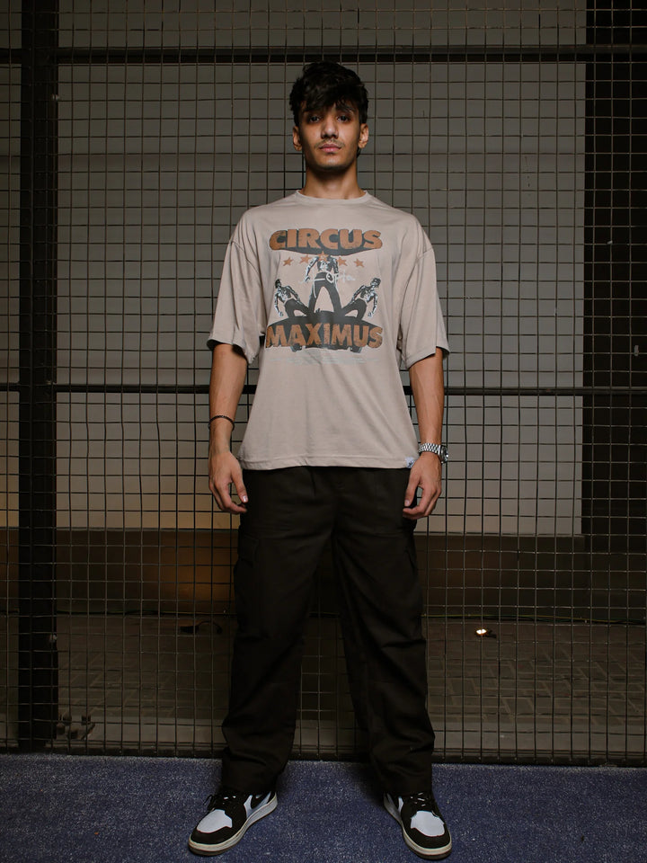 Person wearing a 'Circus Maximus' t-shirt standing against a grid-patterned wall.