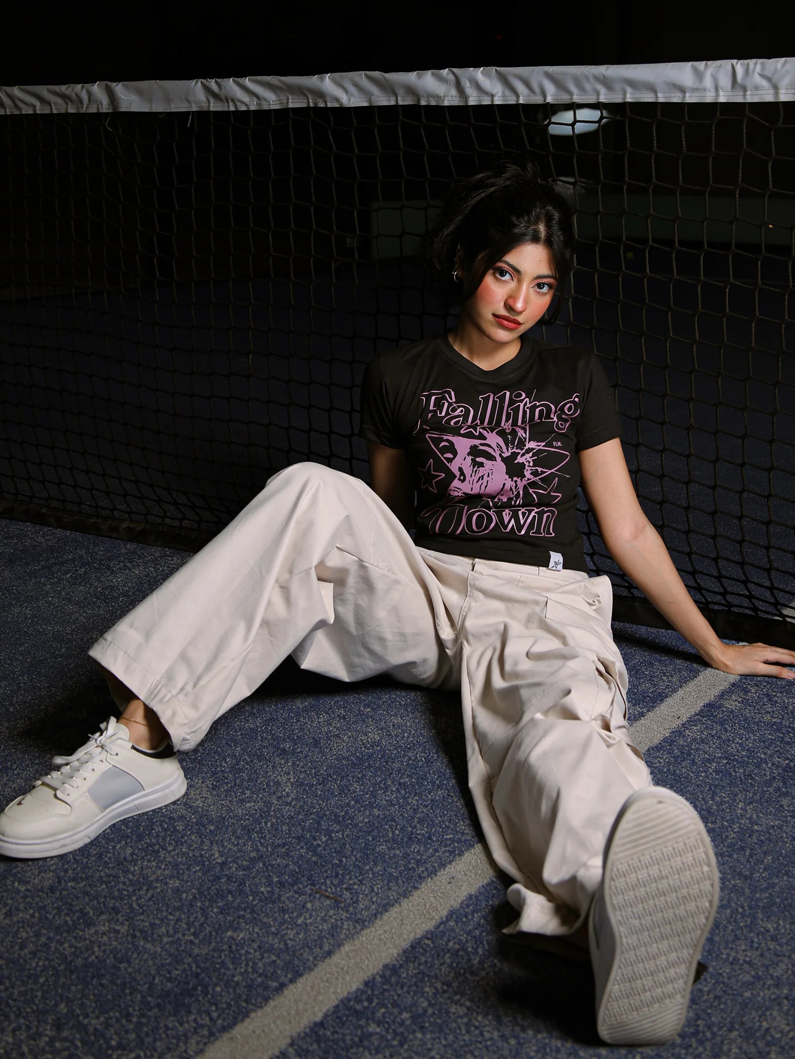 Person sitting on a blue floor wearing a black t-shirt with graphic design and light-colored pants.