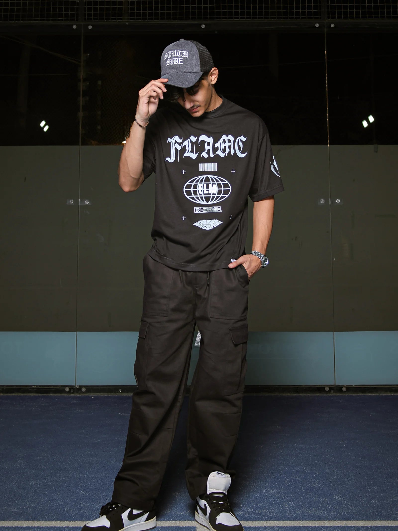 Person wearing a black t-shirt with white text and graphics, standing against a dark wall.
