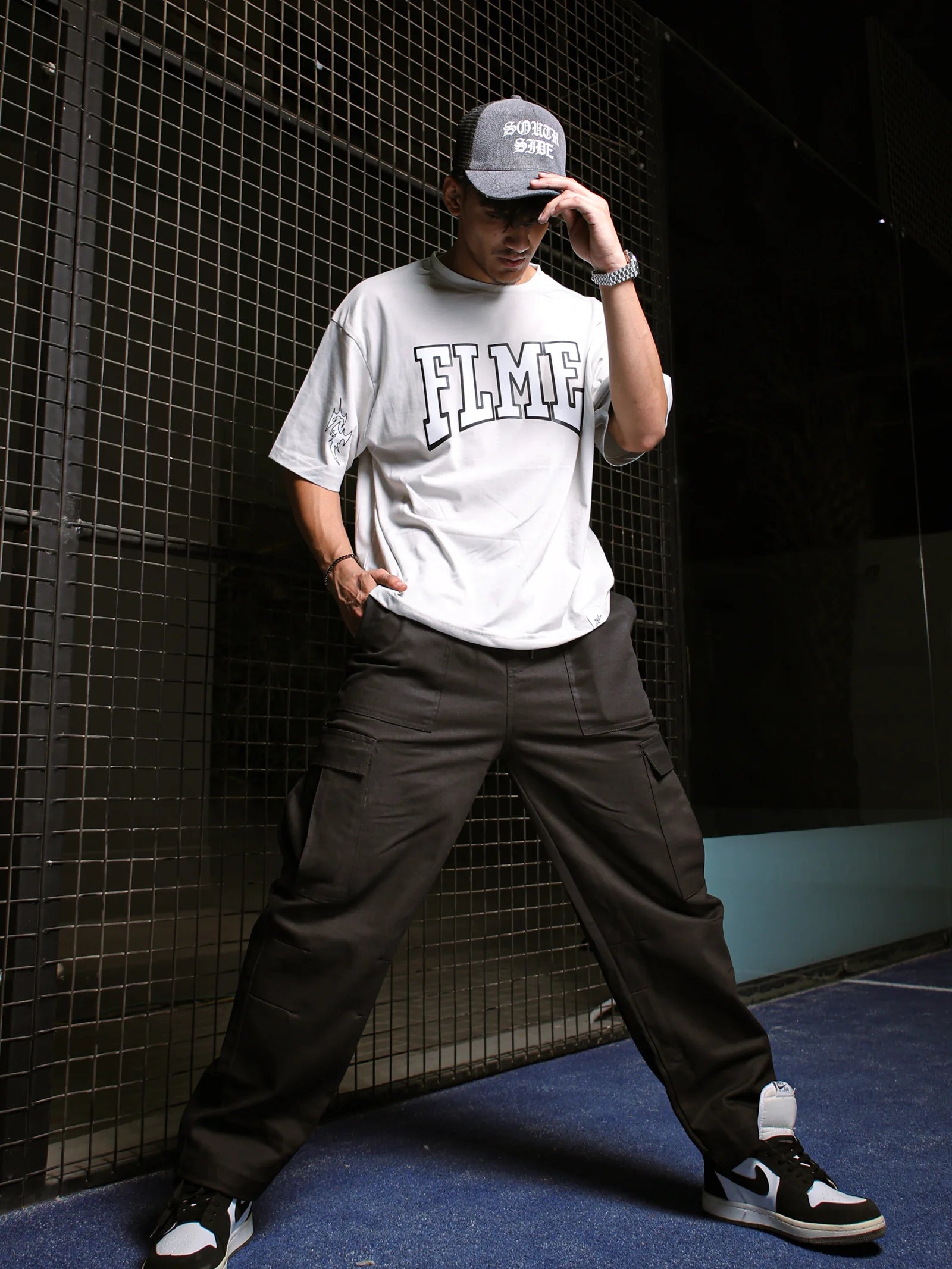 Person wearing a white 'FLME' t-shirt and gray pants against a dark background
