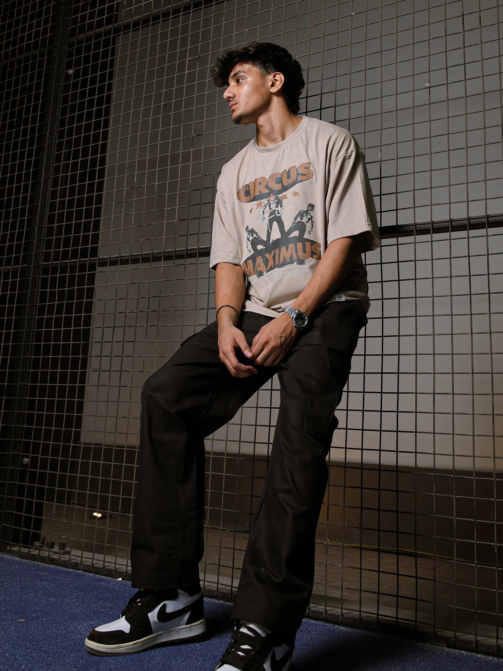 Person wearing a graphic t-shirt and black pants leaning against a tiled wall.