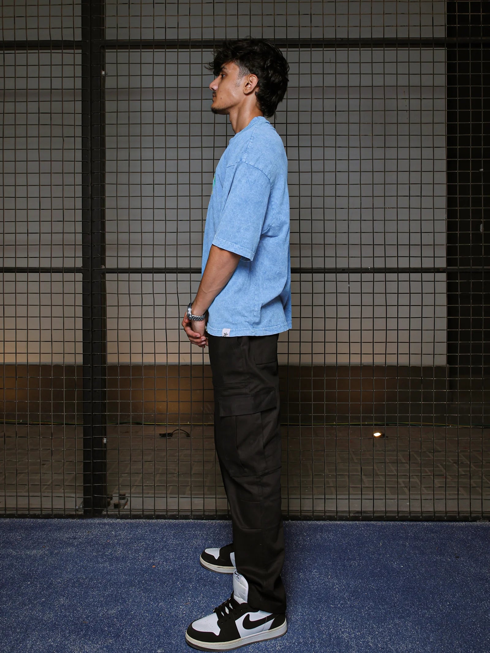 Person wearing a blue shirt and black pants standing against a grid-patterned wall.