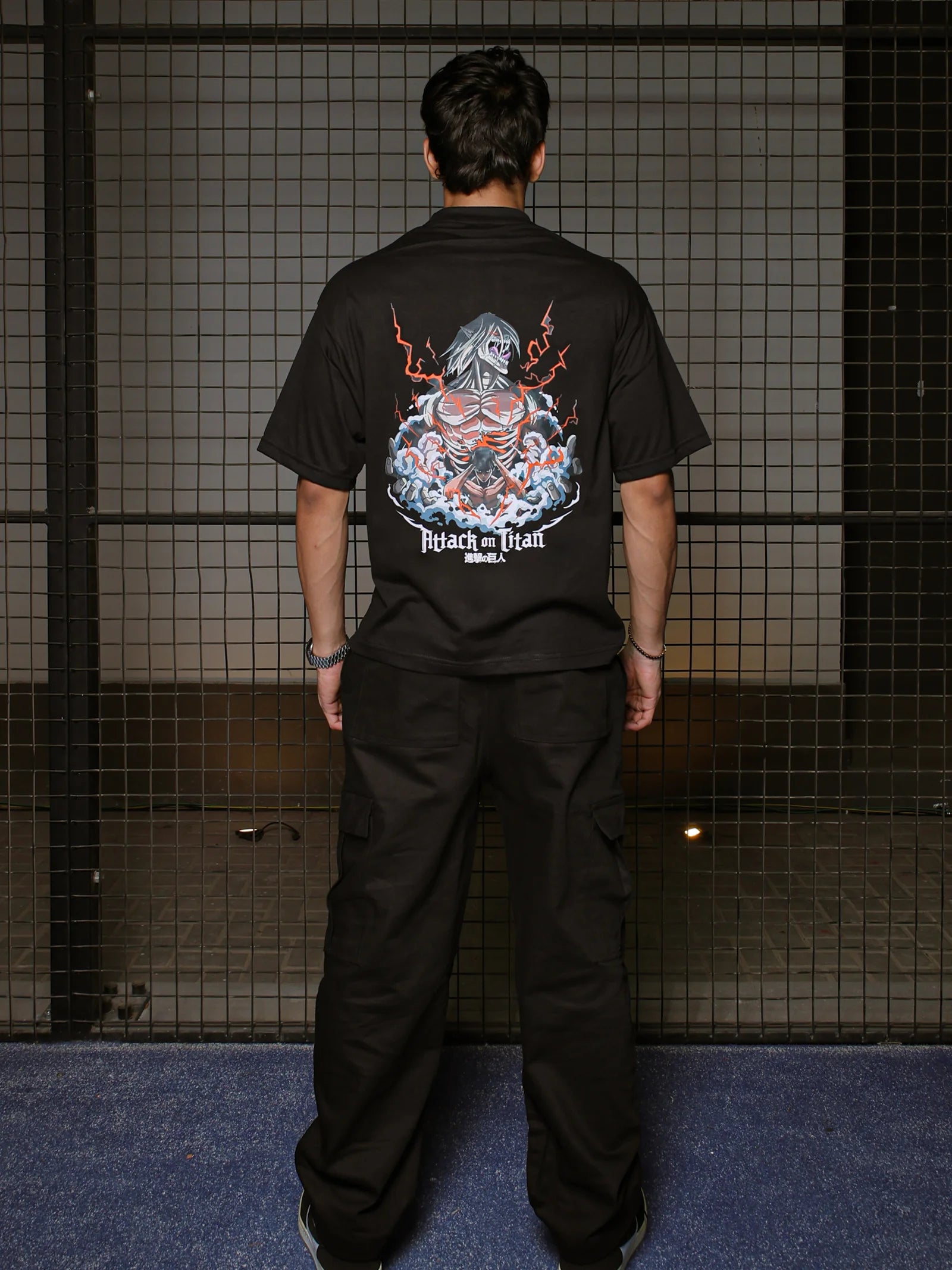 Person wearing a black t-shirt with a graphic design on the back, standing against a grid-patterned wall.