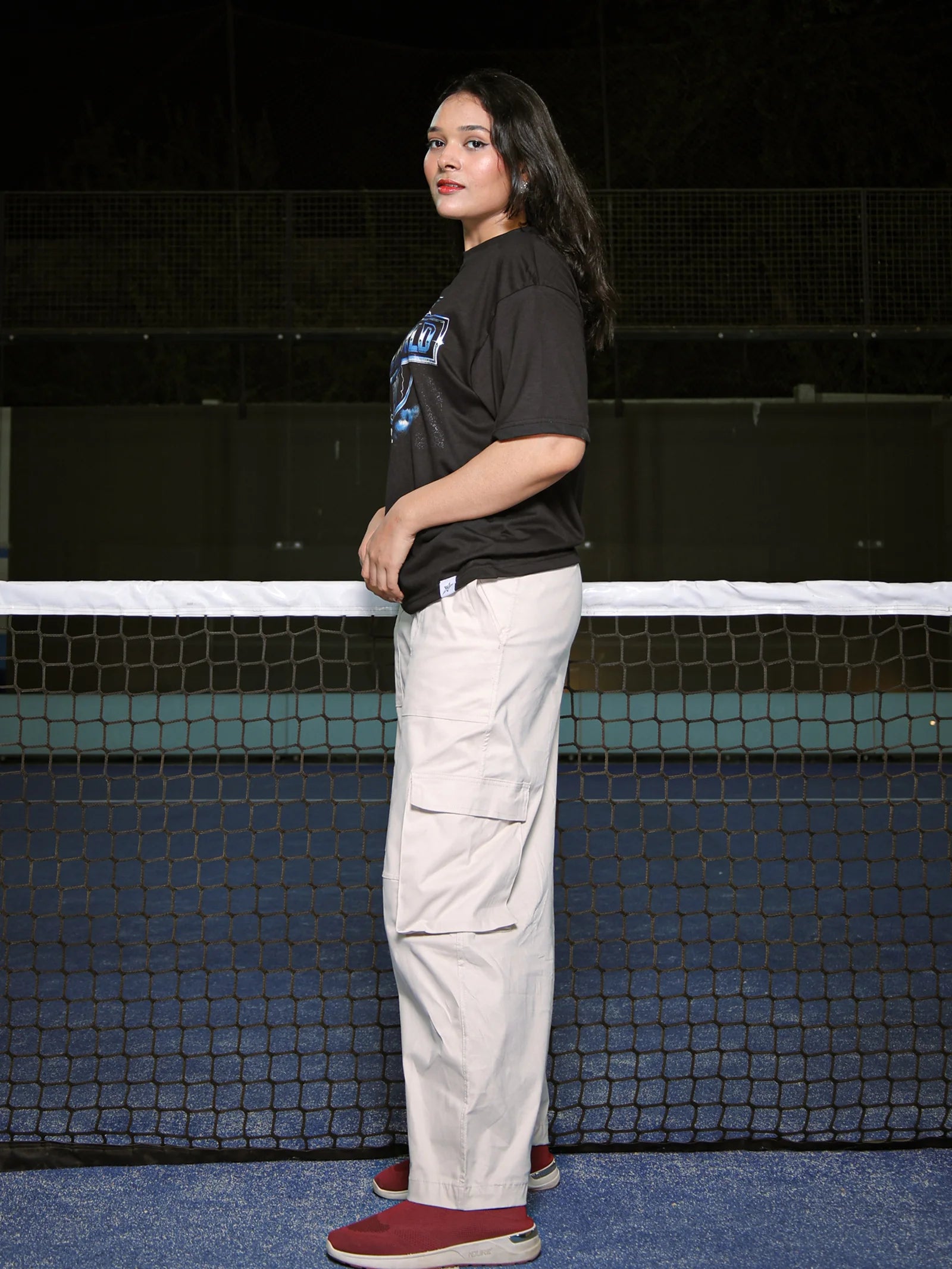 Person standing on a tennis court wearing a black t-shirt and light-colored pants.
