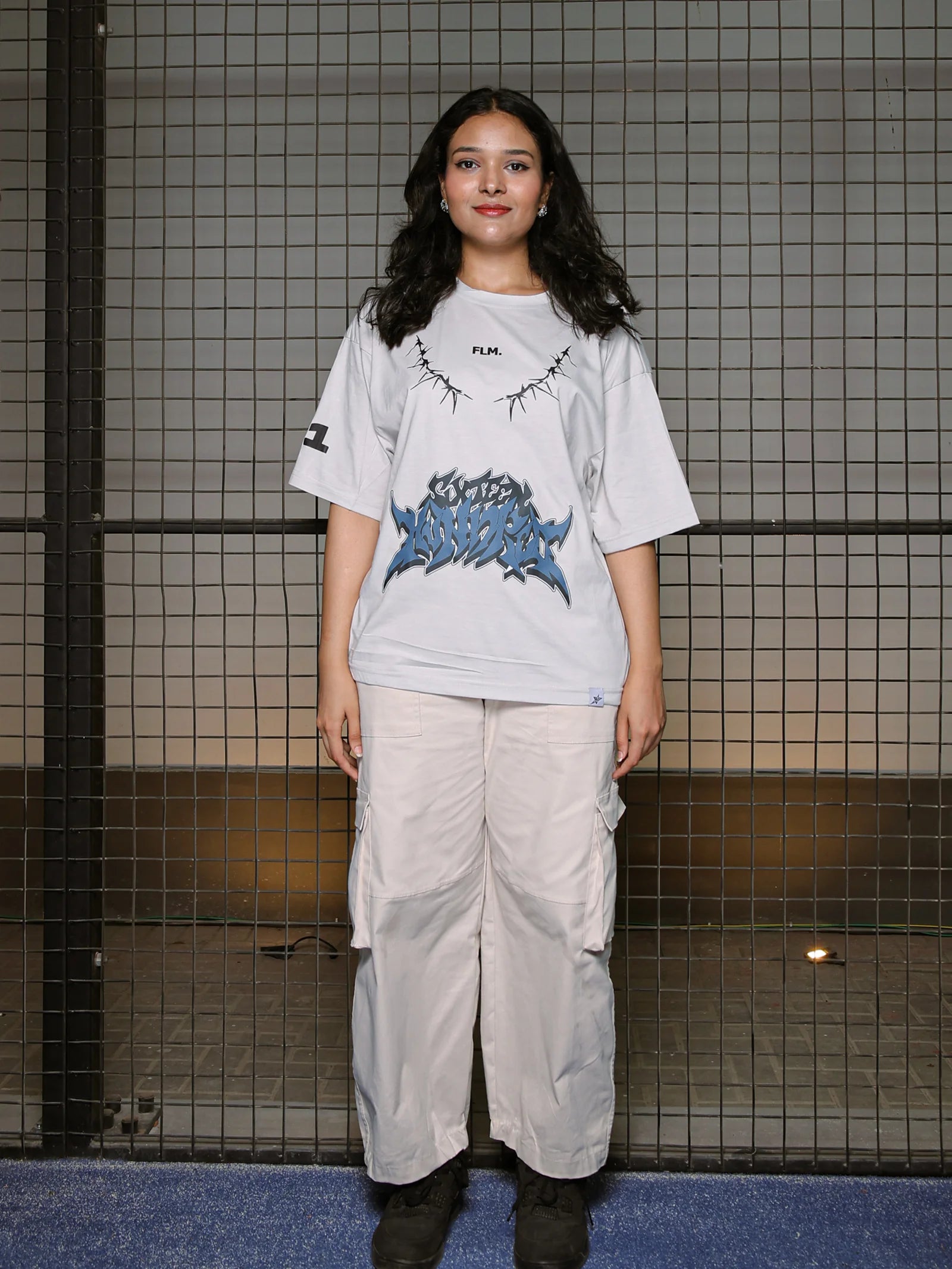 Person wearing a graphic t-shirt and light pants standing against a tiled wall.