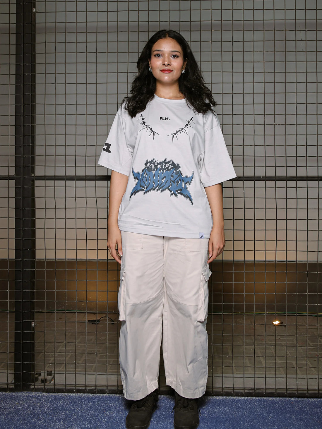 Person wearing a graphic t-shirt and light pants standing against a tiled wall.