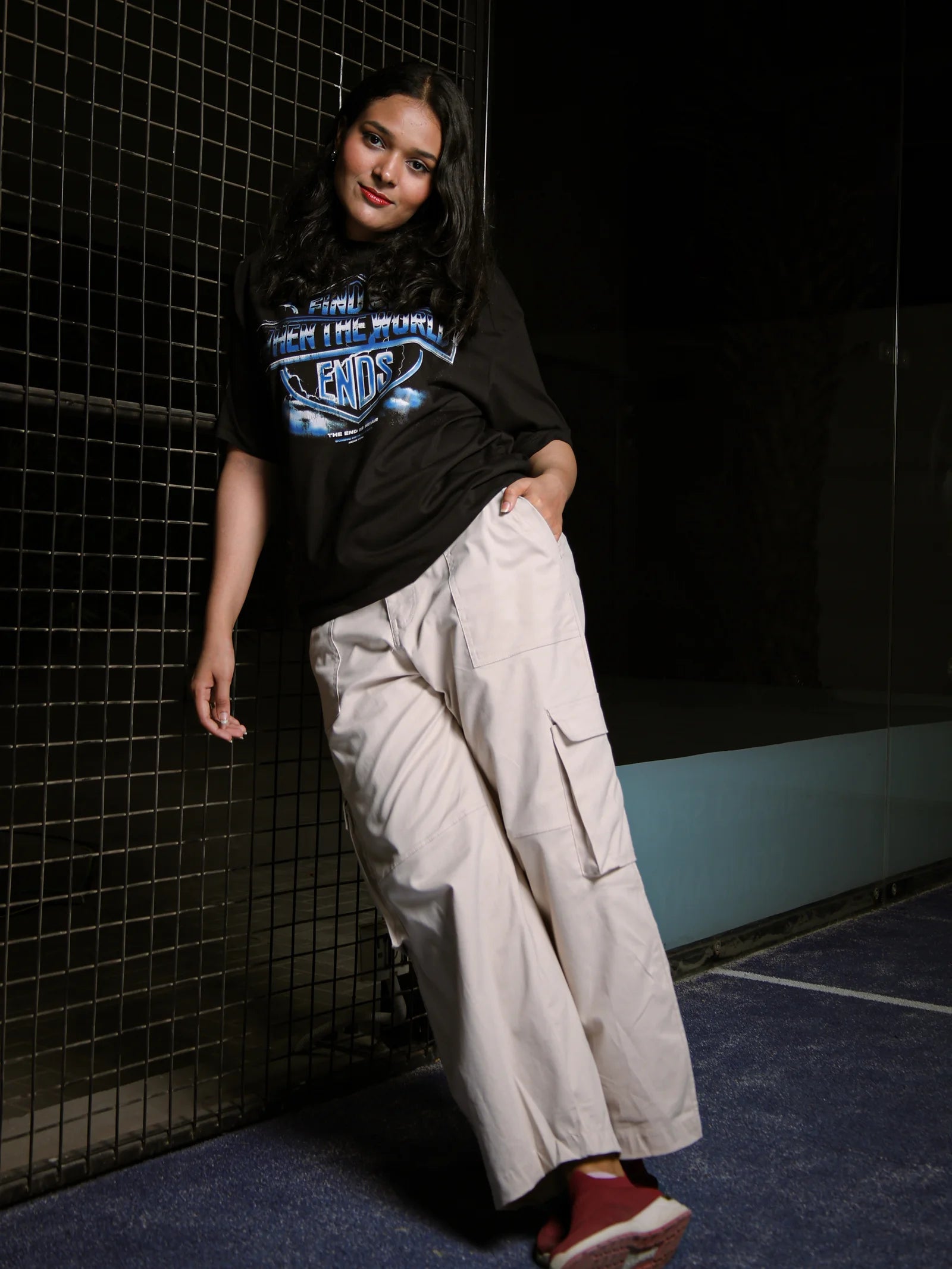 Person wearing a black t-shirt with graphic design and light-colored pants against a dark tiled wall.