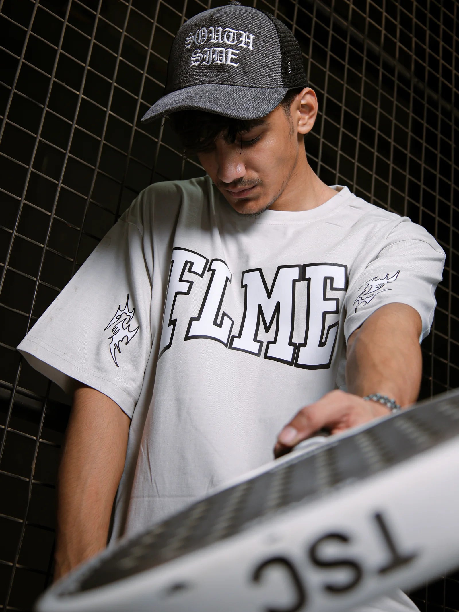 Person wearing a gray cap and white t-shirt with 'FLMIE' branding, holding a metallic object.