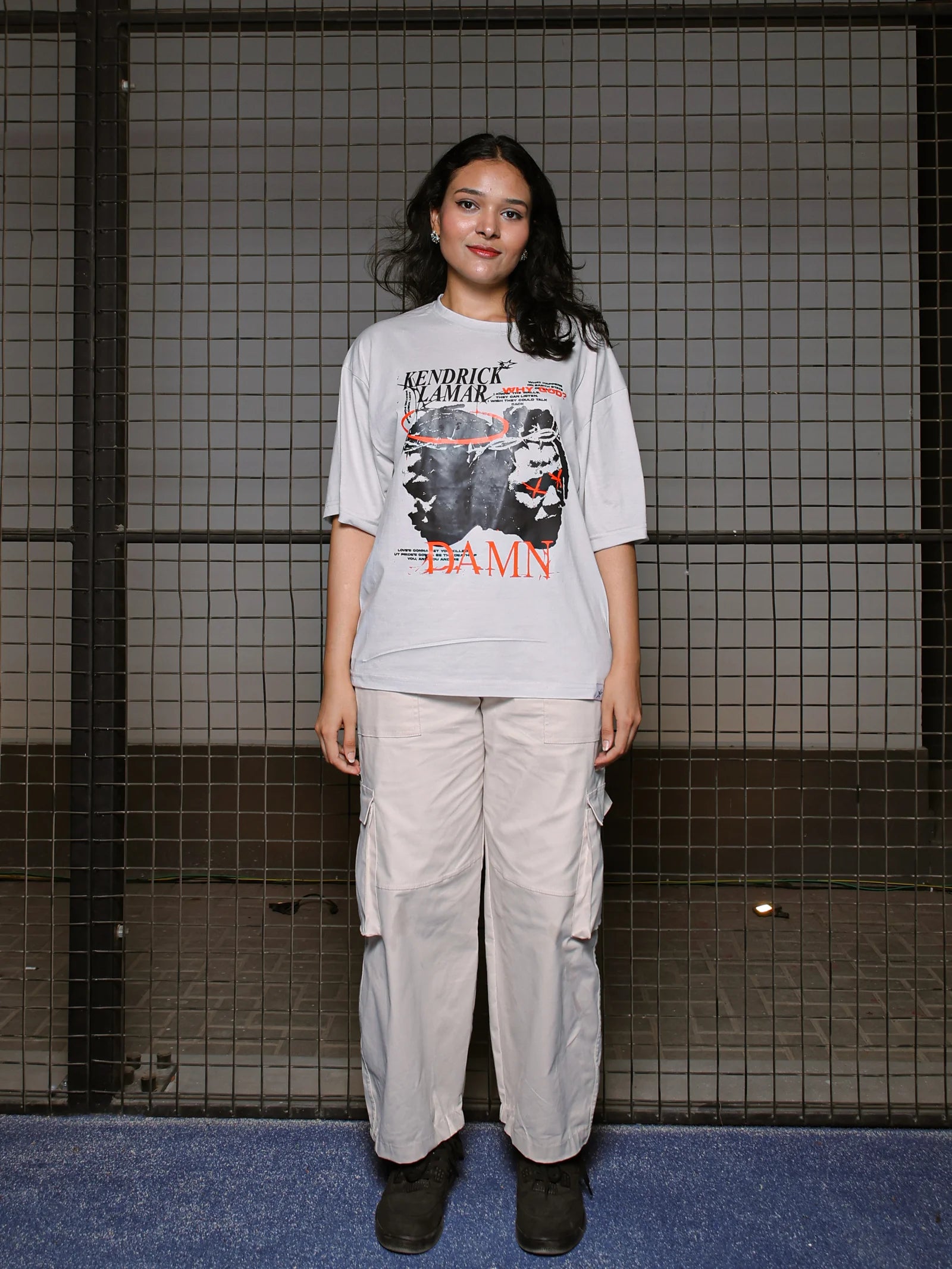 Person wearing a graphic t-shirt and cargo pants standing against a tiled wall.