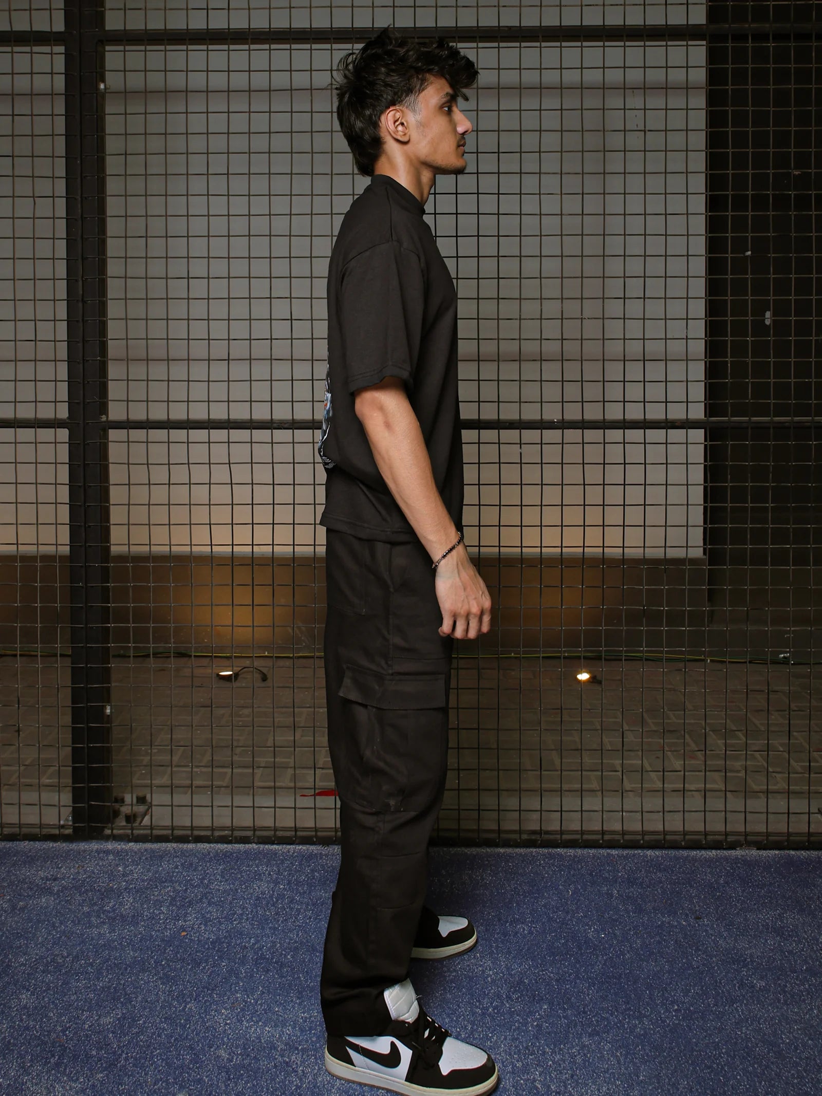 Person wearing a black outfit with a Nike sneaker standing against a dark grid background