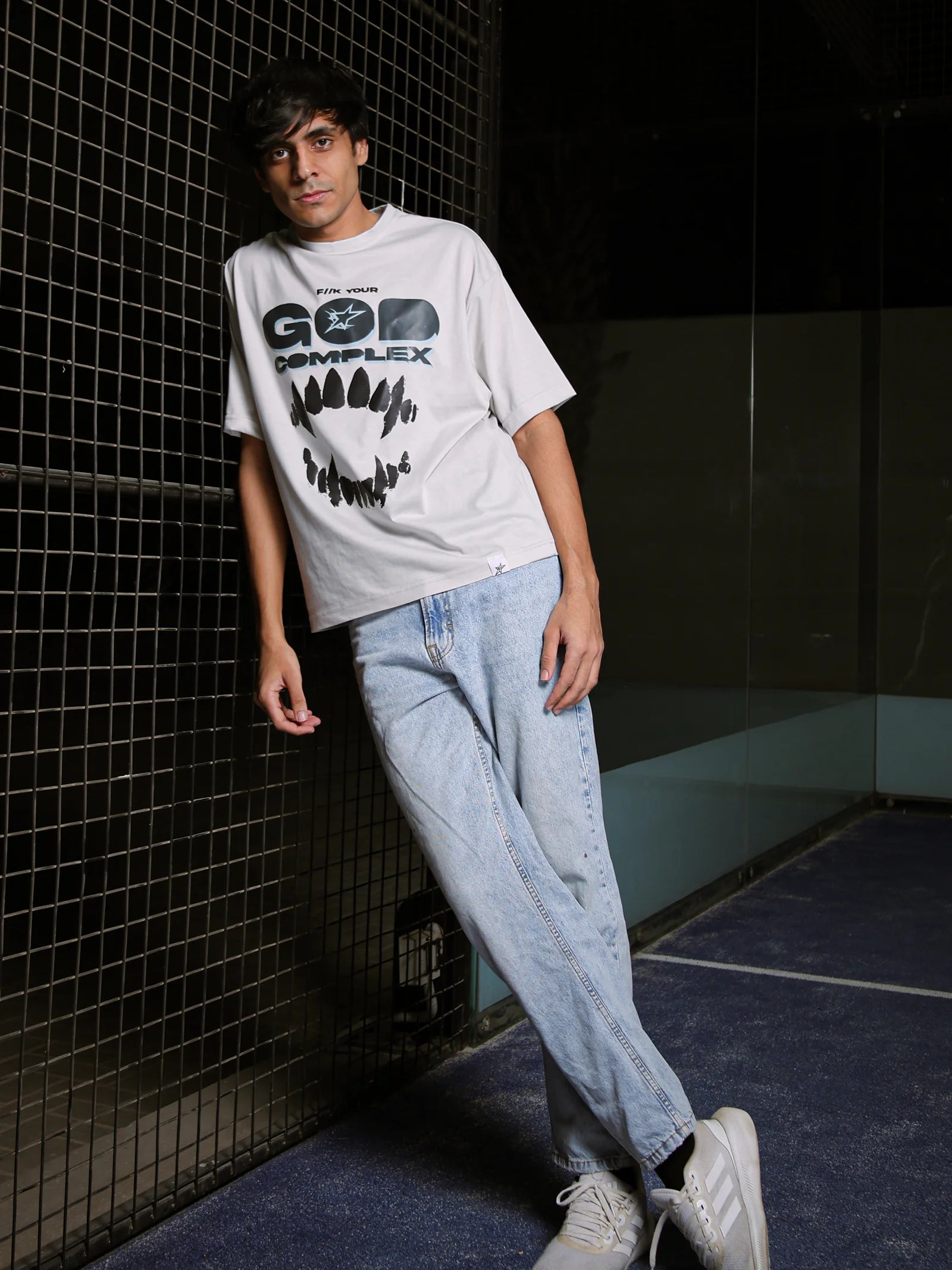 Person wearing a white t-shirt with text and graphics, standing against a dark tiled wall.