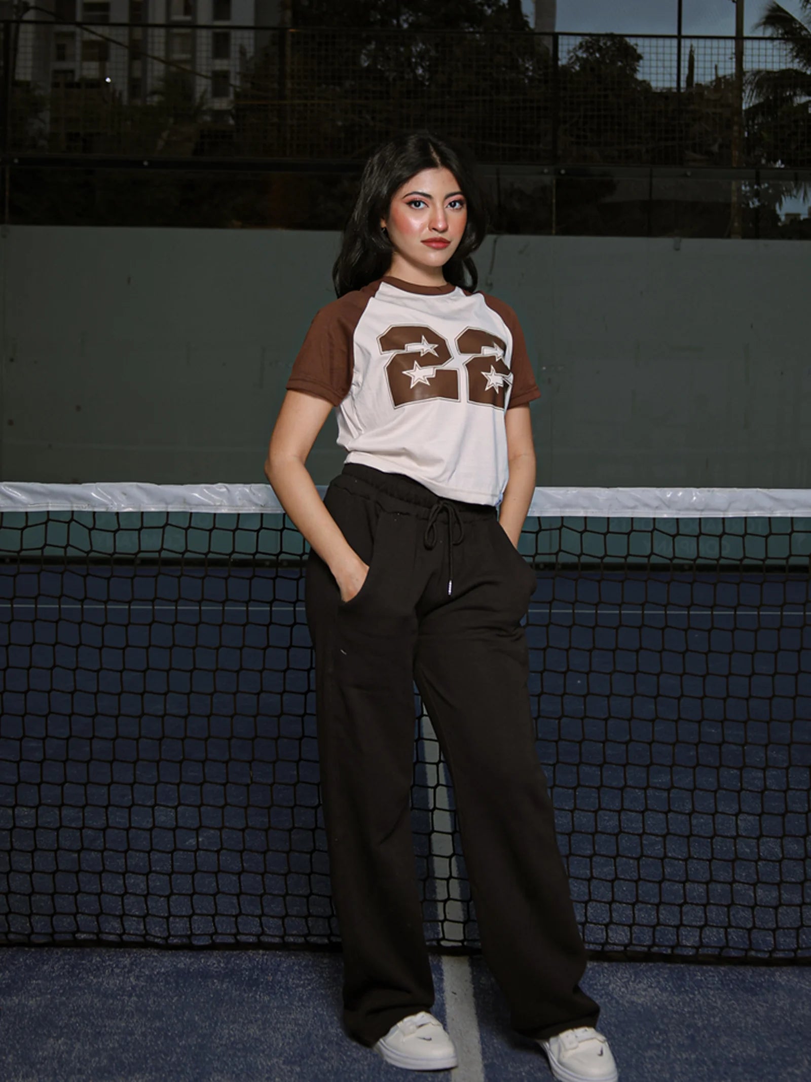 Person wearing a brown and white t-shirt with number 22 and dark pants standing on a tennis court.