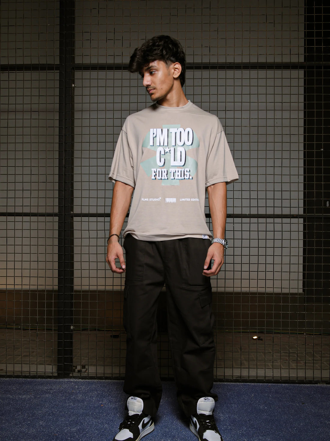 Person wearing a beige t-shirt with text and black pants standing against a grid-patterned wall.