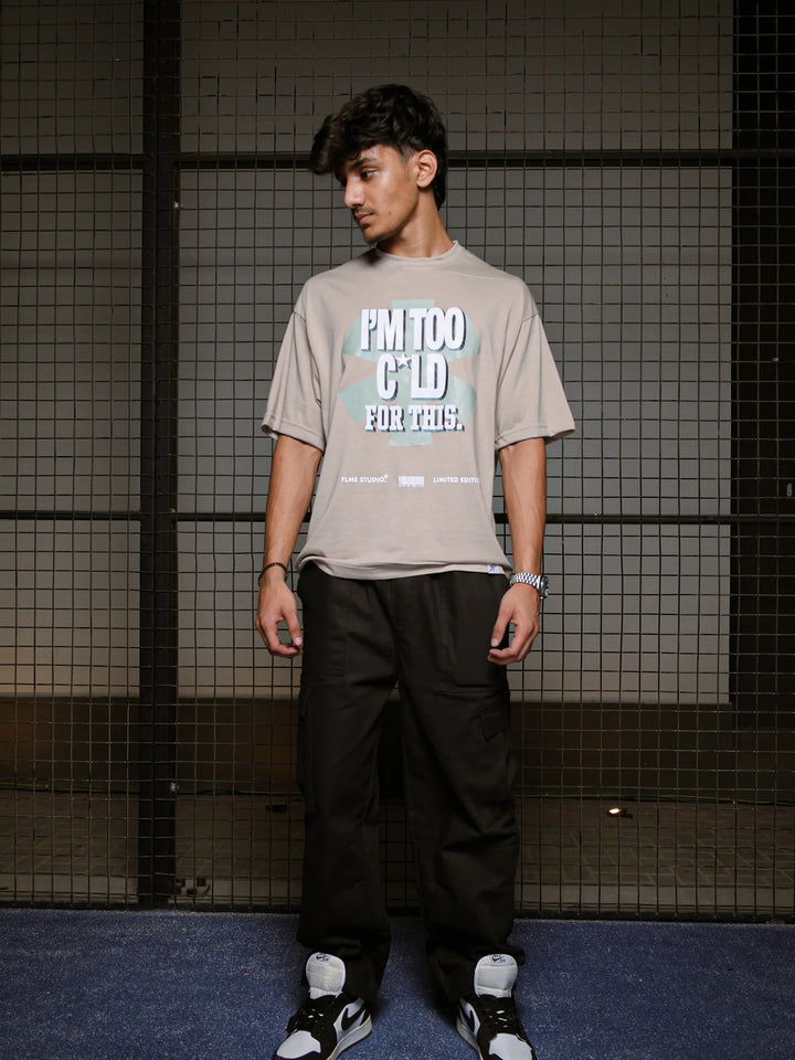 Person wearing a beige t-shirt with text and black pants standing against a grid-patterned wall.