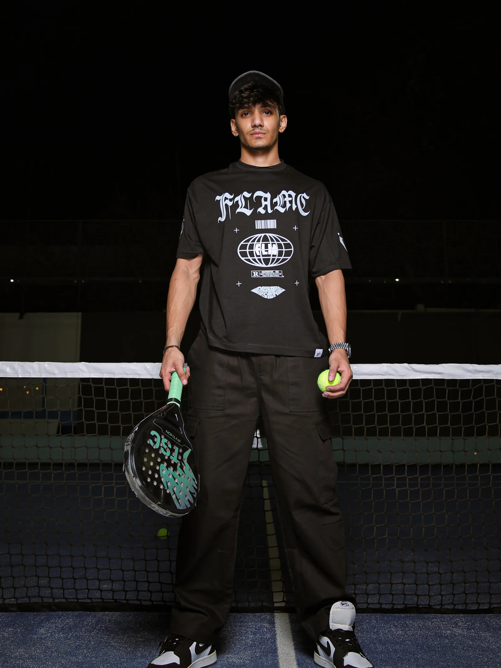 Person holding a paddle and ball on a tennis court at night
