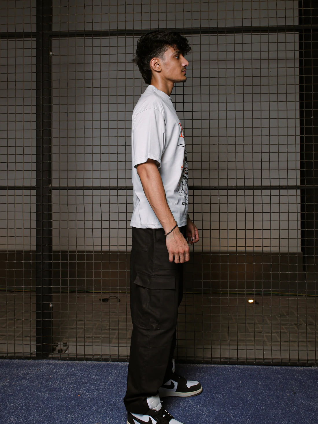 Person wearing a white t-shirt and black pants standing against a tiled wall.