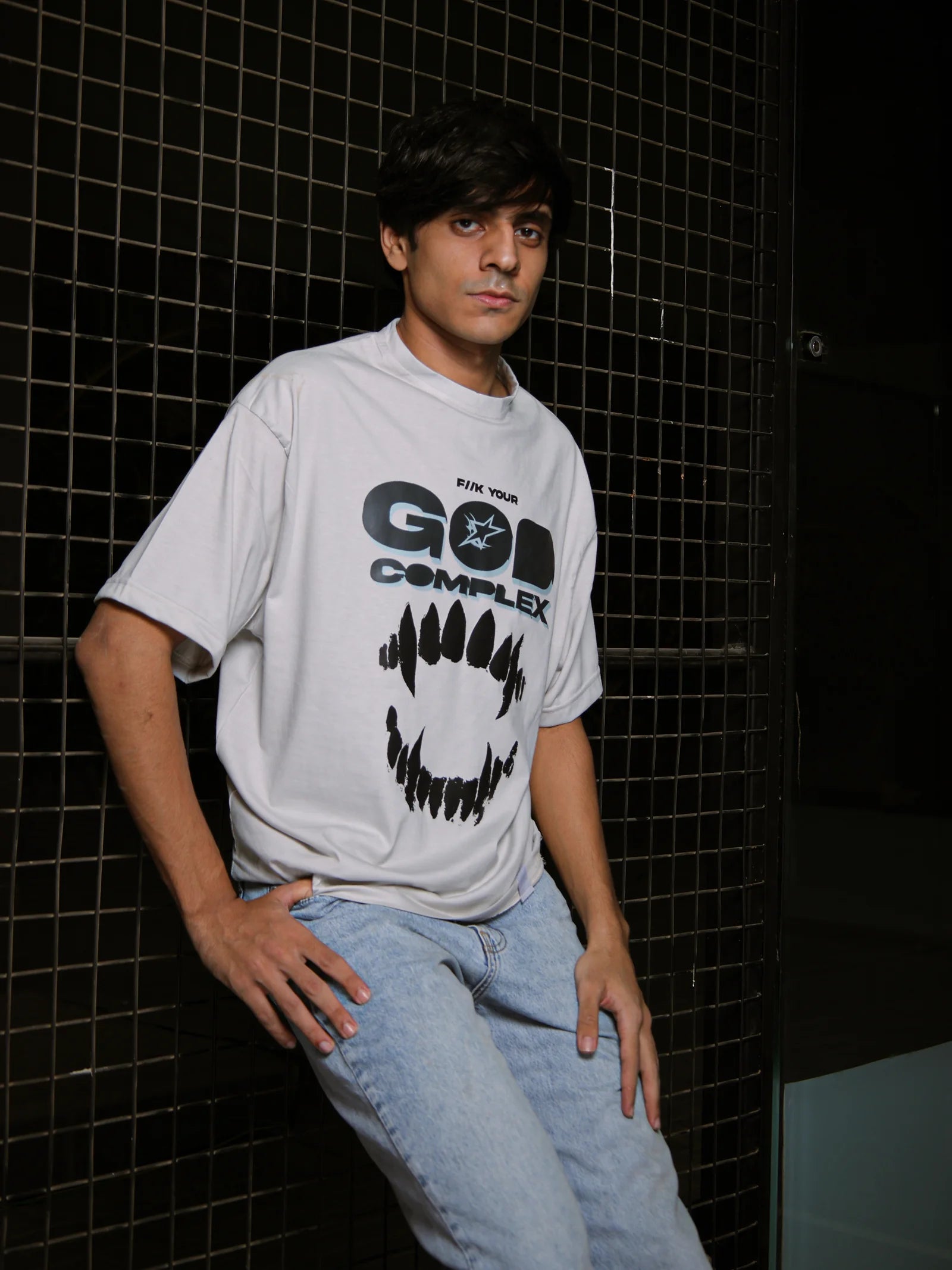 Person wearing a white t-shirt with text and graphics against a dark tiled wall.