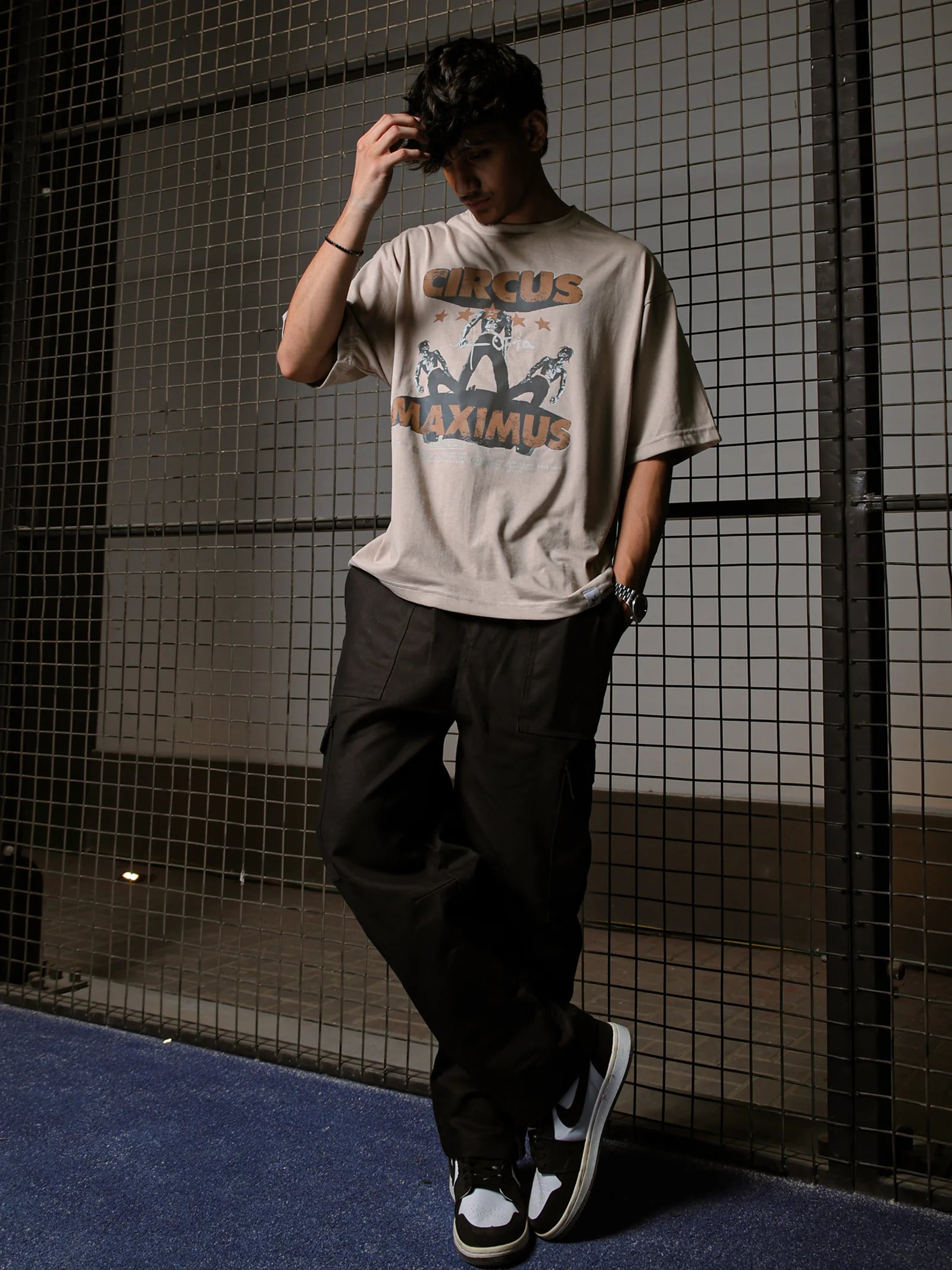 Person wearing a graphic t-shirt and dark pants standing against a tiled wall.