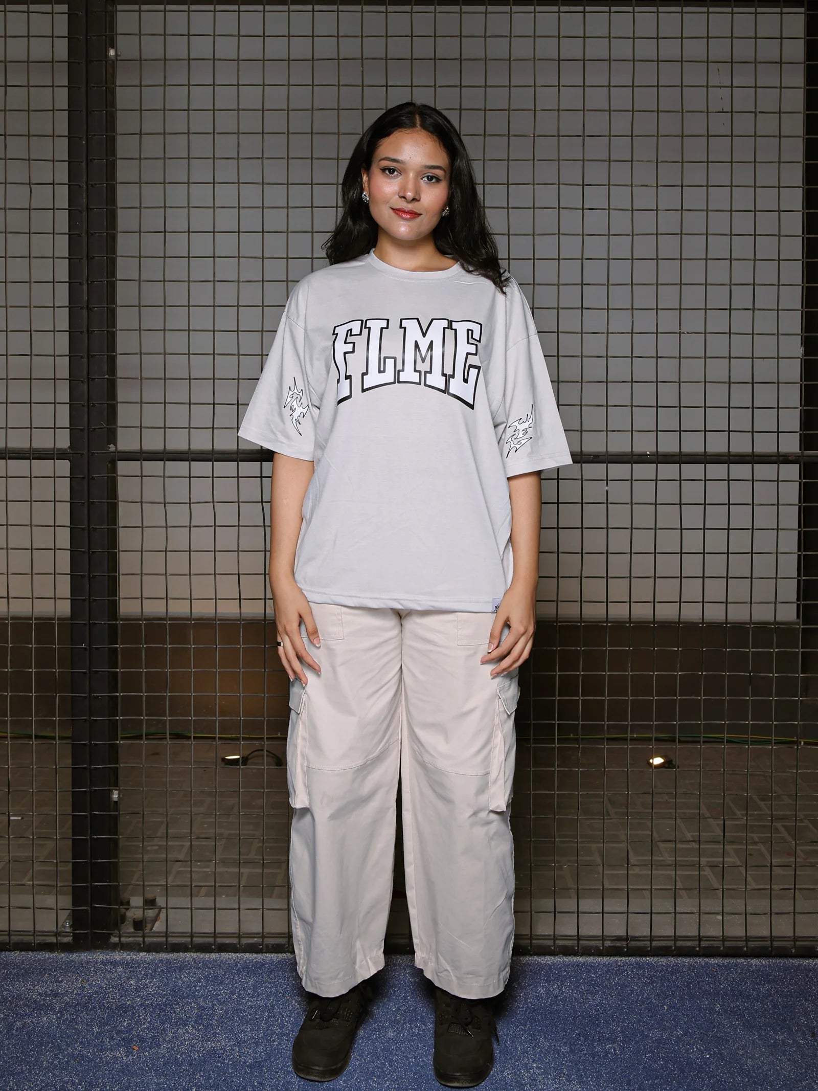 Person wearing a gray oversized t-shirt with 'FLME' branding and beige cargo pants in a tiled room.