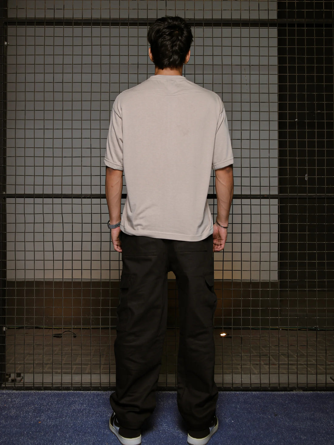 Person wearing a beige t-shirt and black pants standing in front of a tiled wall.