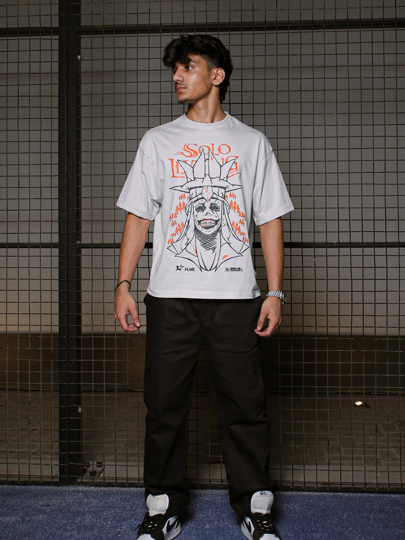 Person wearing a gray t-shirt with a graphic design against a tiled wall.