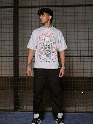 Person wearing a gray t-shirt with a graphic design against a tiled wall.