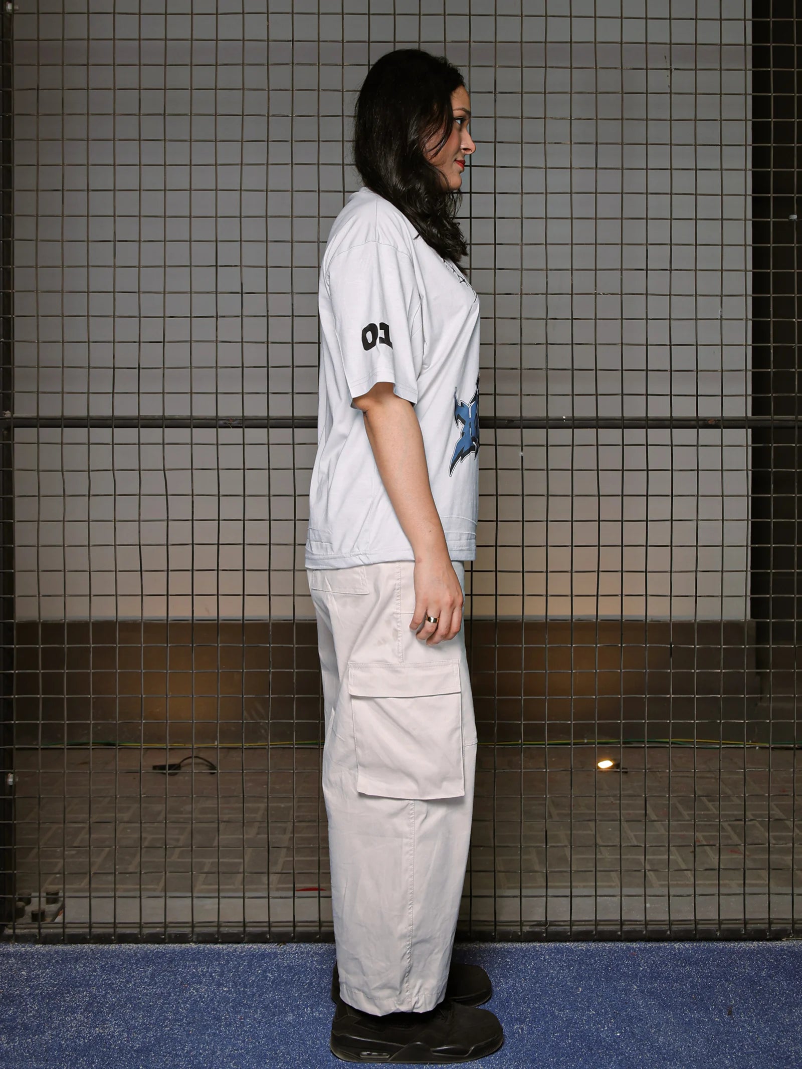 Person wearing a light blue t-shirt and beige pants standing against a tiled wall.
