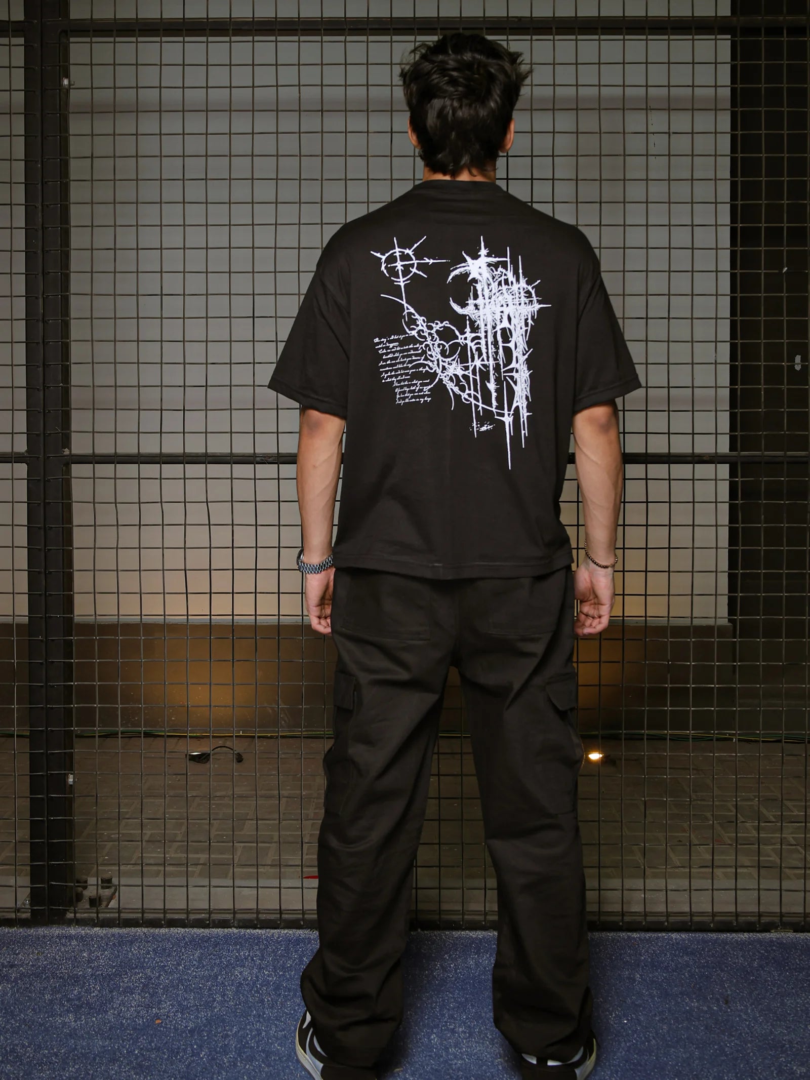 Person wearing a black t-shirt with white graphic design in front of a grid-patterned wall.