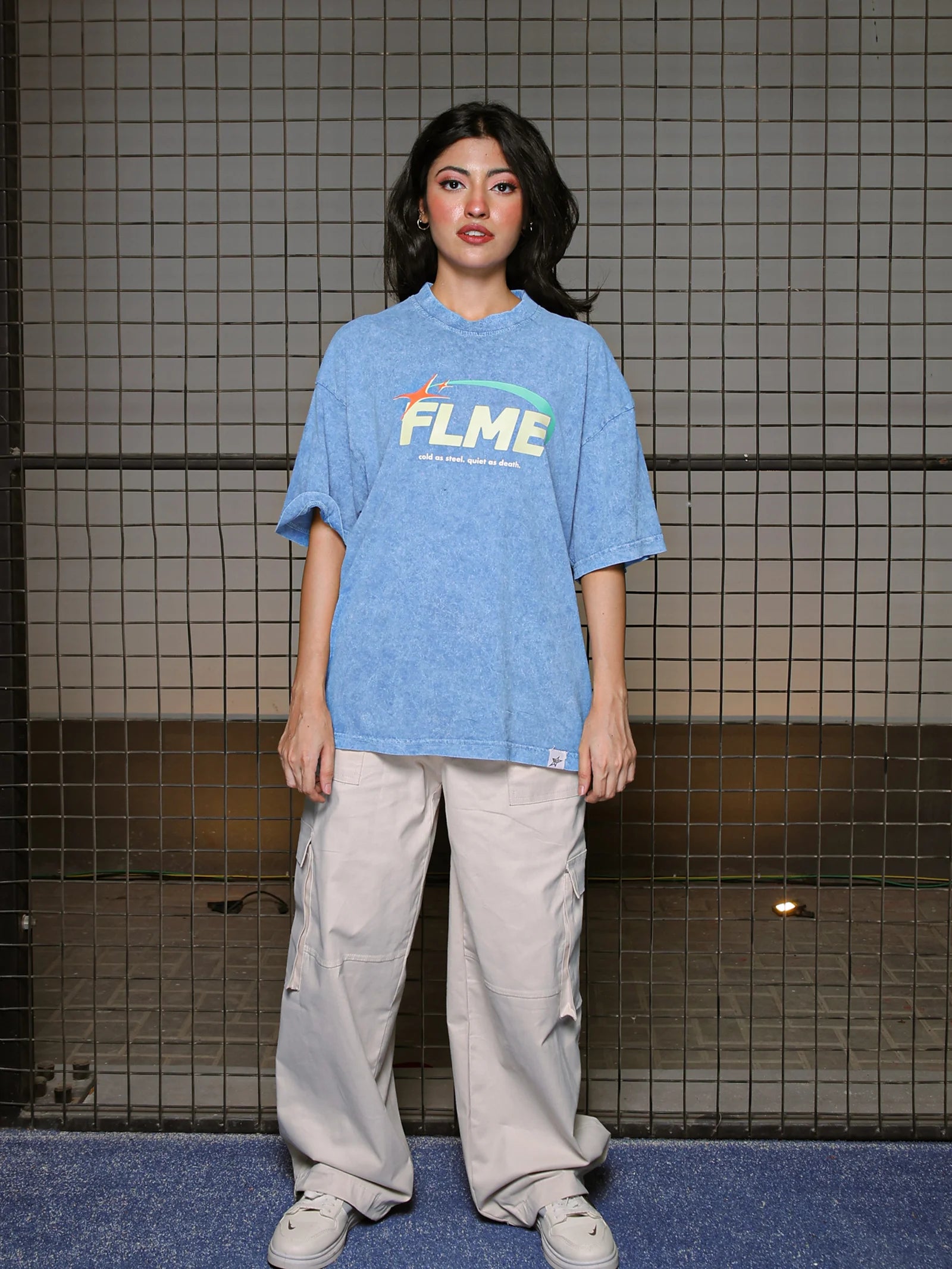 Person wearing a blue t-shirt with 'FLME' logo against a tiled wall.