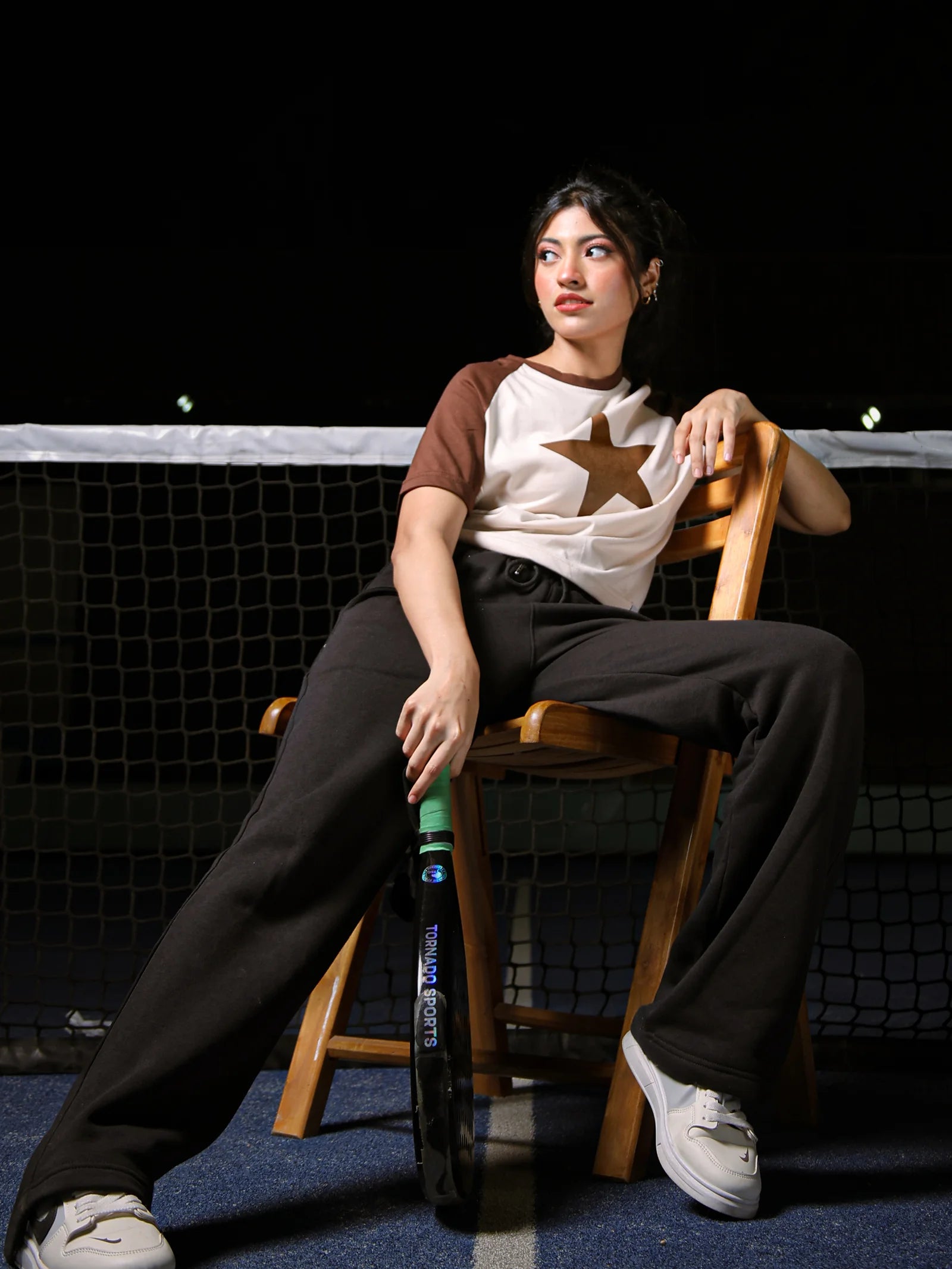 Person sitting on a chair holding a tennis racket on a tennis court at night.