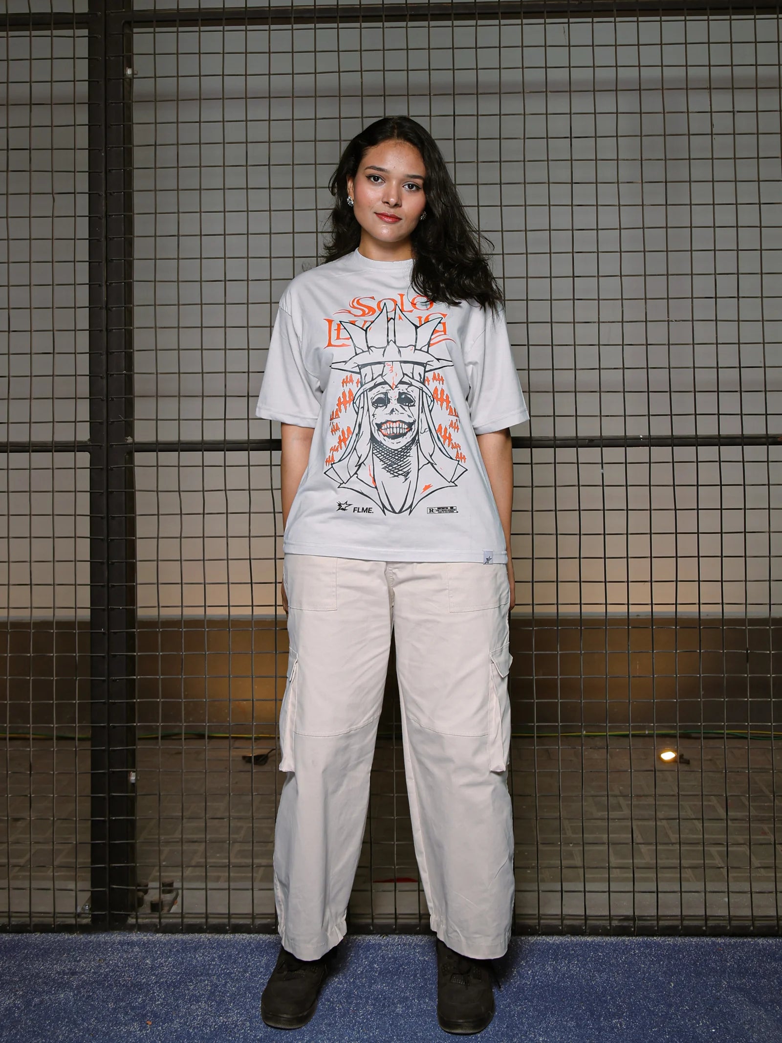 Person wearing a graphic t-shirt and light-colored pants standing against a tiled wall.