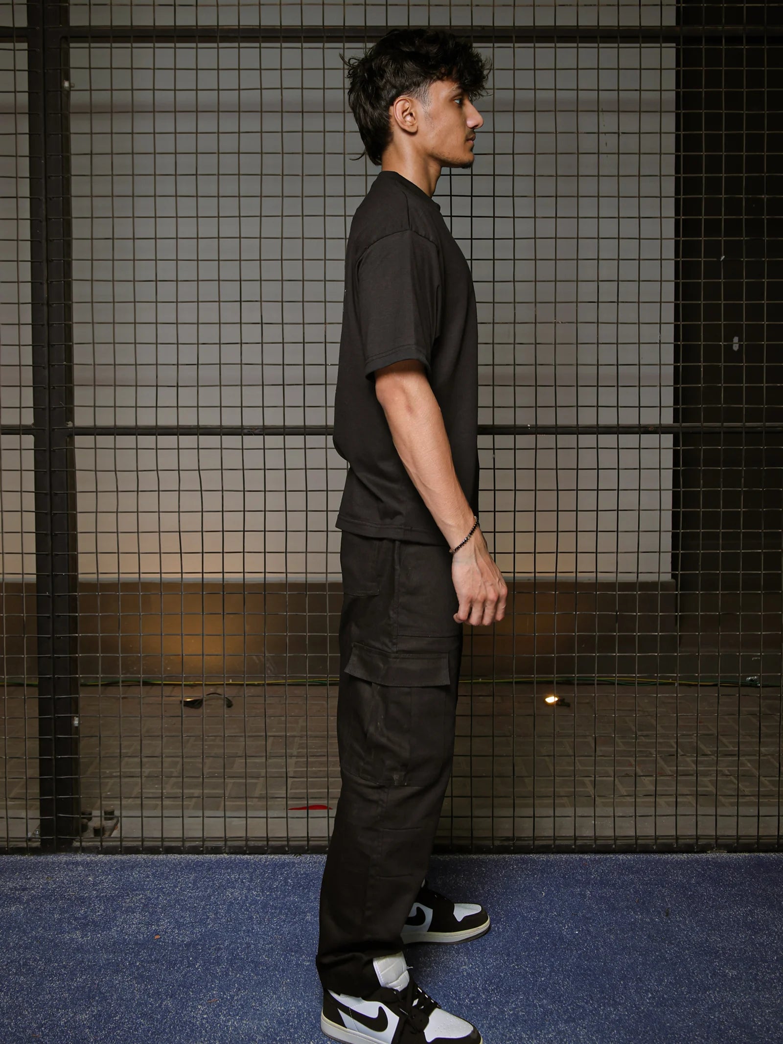 Person wearing a black outfit with Nike shoes standing against a grid-patterned wall.