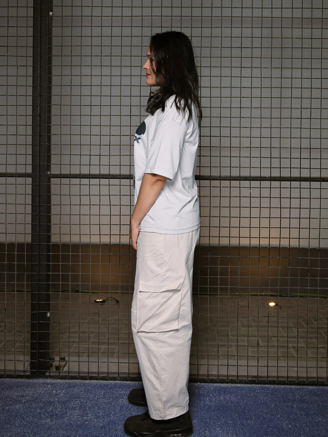 Person wearing a white t-shirt and beige pants standing against a tiled wall.