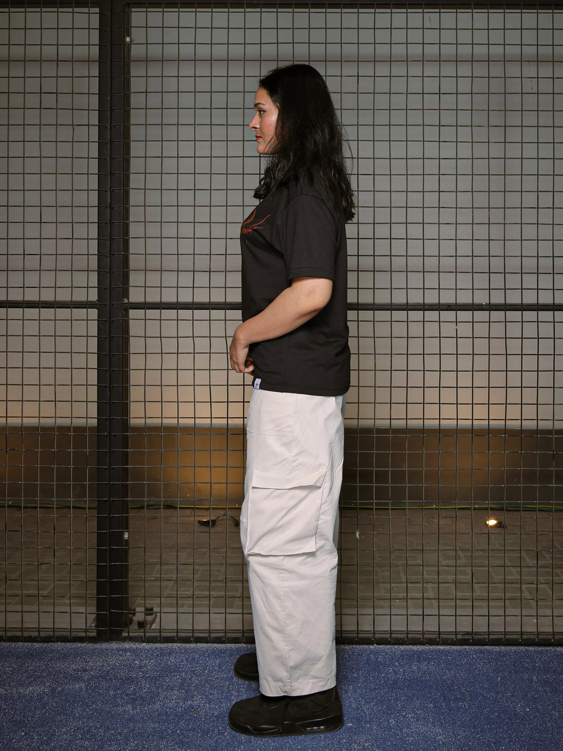 Person wearing a black shirt and light gray pants standing against a tiled wall.