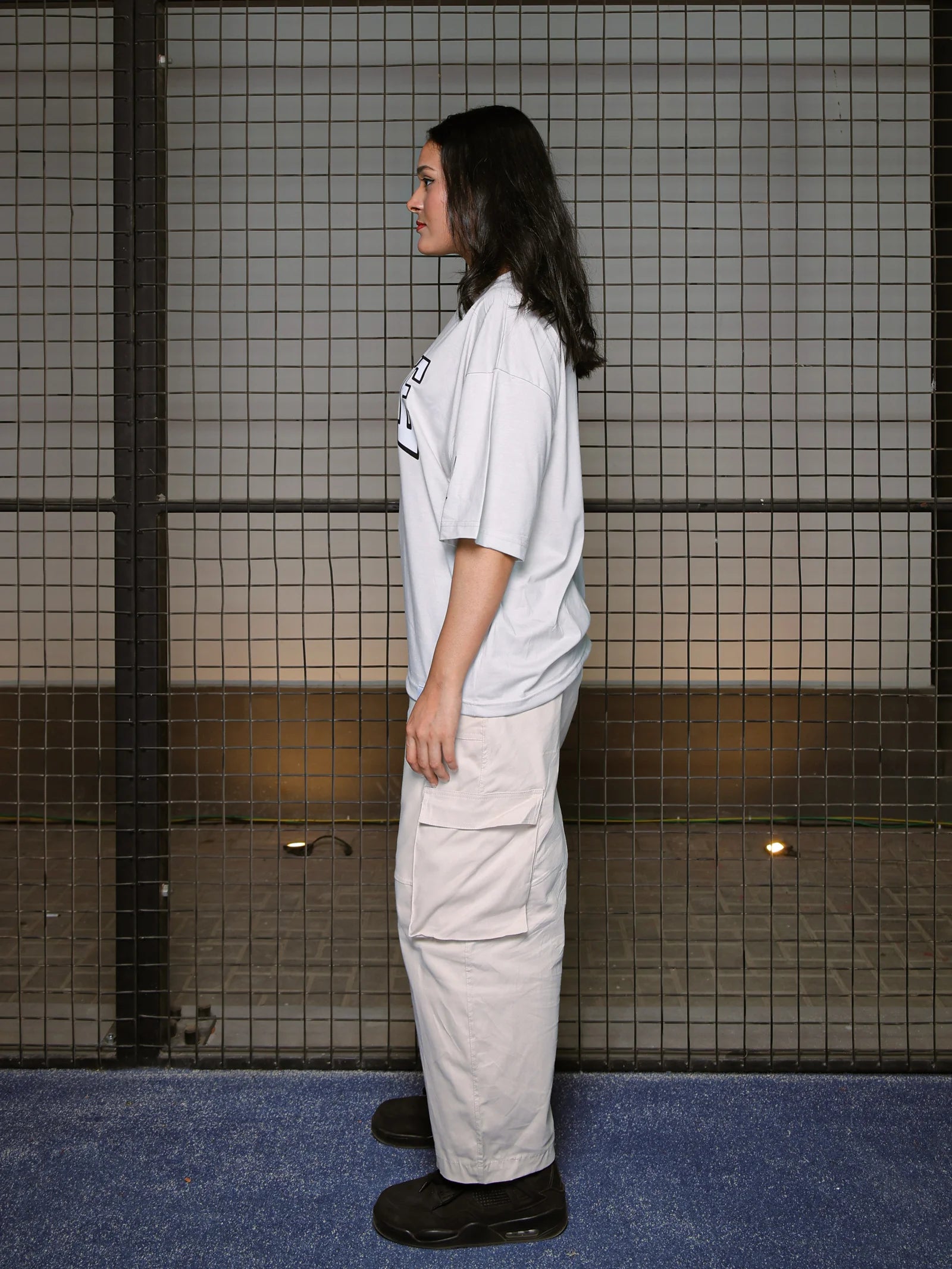 Person wearing a white t-shirt and beige pants standing against a tiled wall.