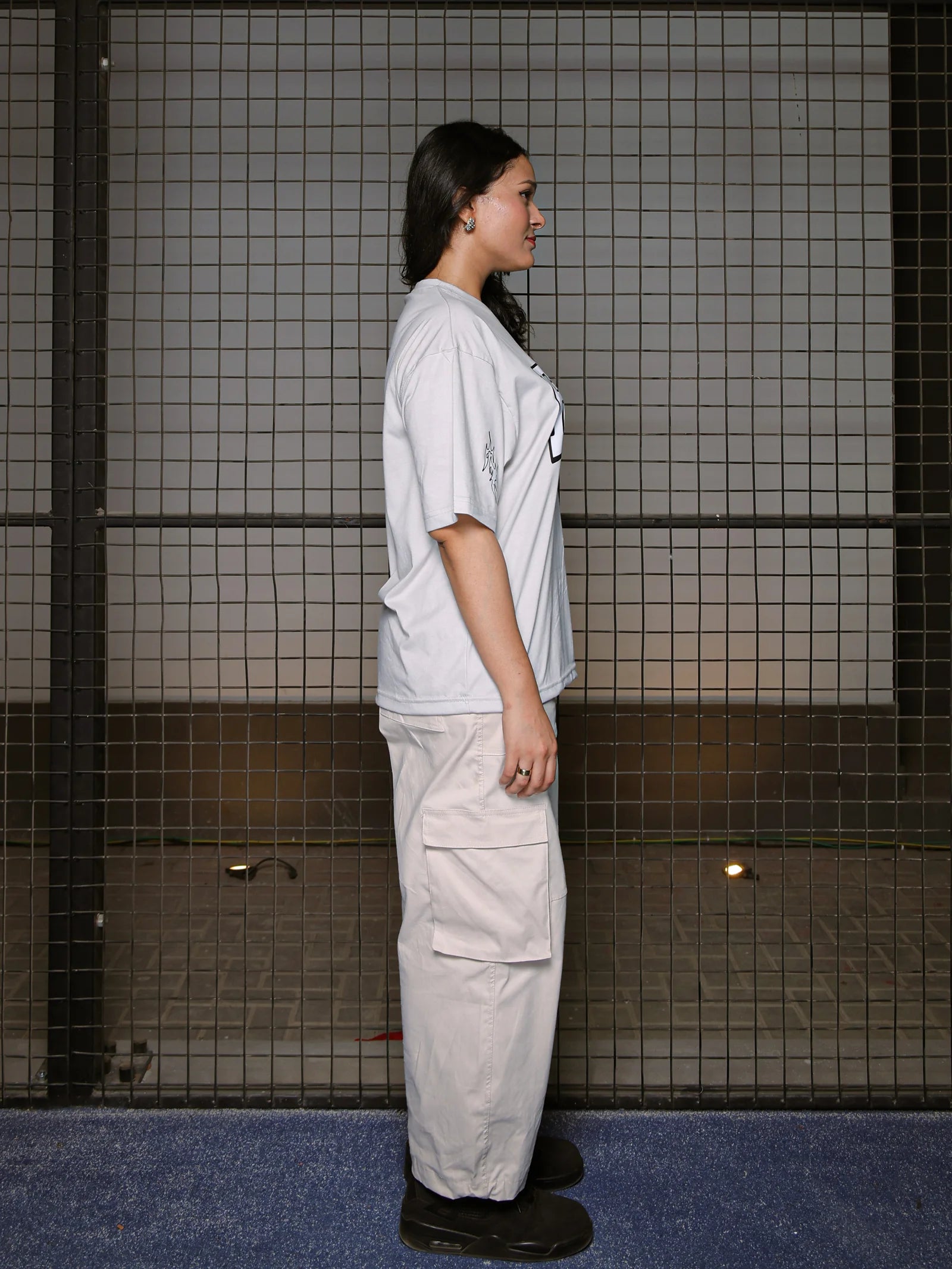 Person wearing a light gray t-shirt and beige pants standing in a tiled room.