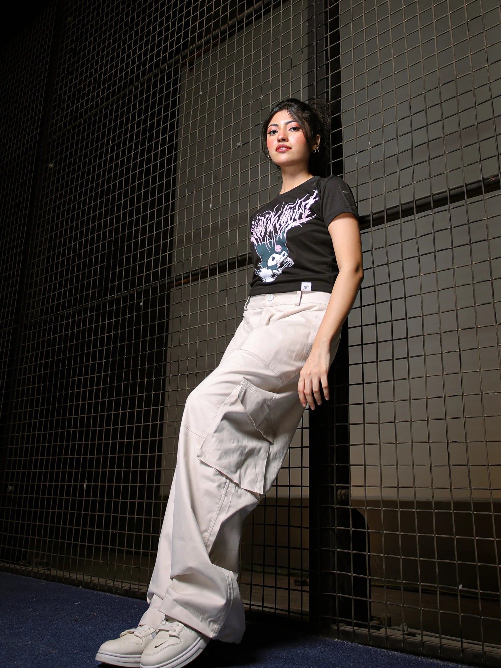 Person wearing a black t-shirt and light-colored pants standing against a dark tiled wall.
